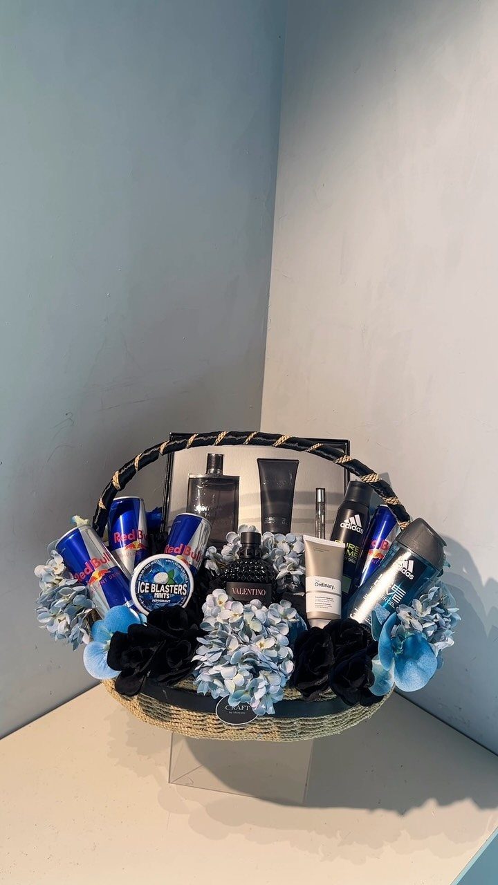Wicker gift basket filled with men's grooming products and blue and black flowers.