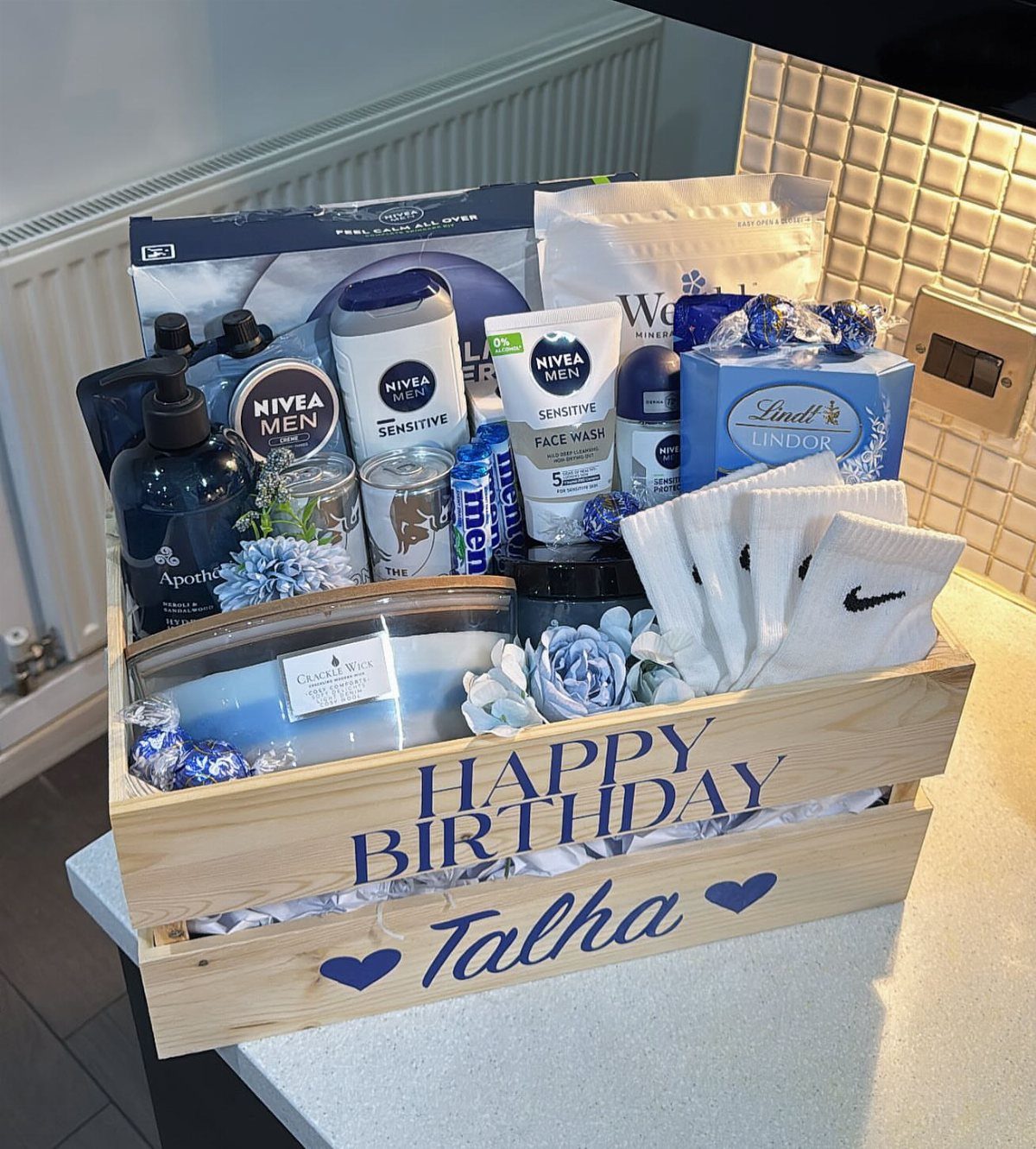 Wooden birthday gift crate filled with men's skincare, chocolates, and white socks.