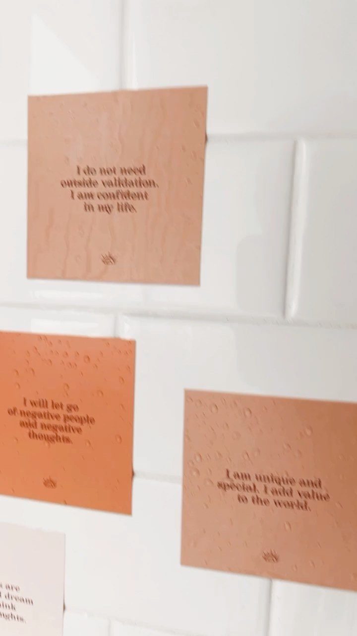 Peach-colored affirmation cards with positive quotes stuck to a white tiled wall.