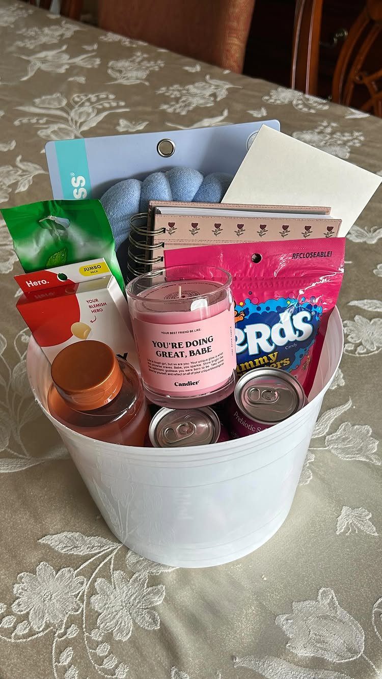 White bucket filled with a pink candle, candy, and notebooks on floral tablecloth.