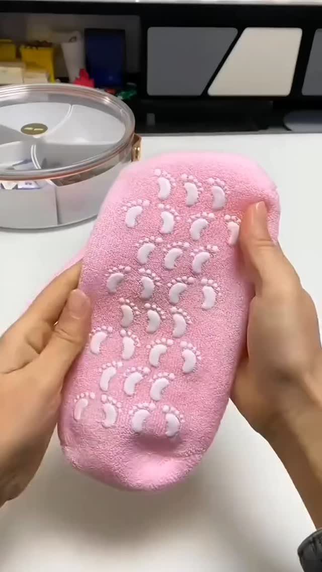 Fluffy pink sock with white non-slip footprint grips held by two hands.