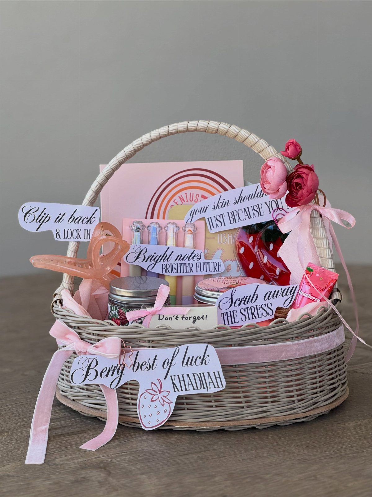 Woven gift basket filled with pink stationery, skincare jars, and decorative floral accents.