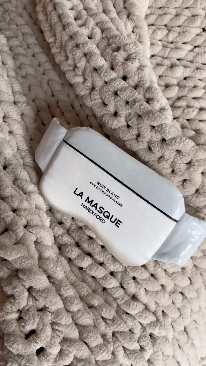 White fabric sleep mask resting on a chunky cream knitted blanket.