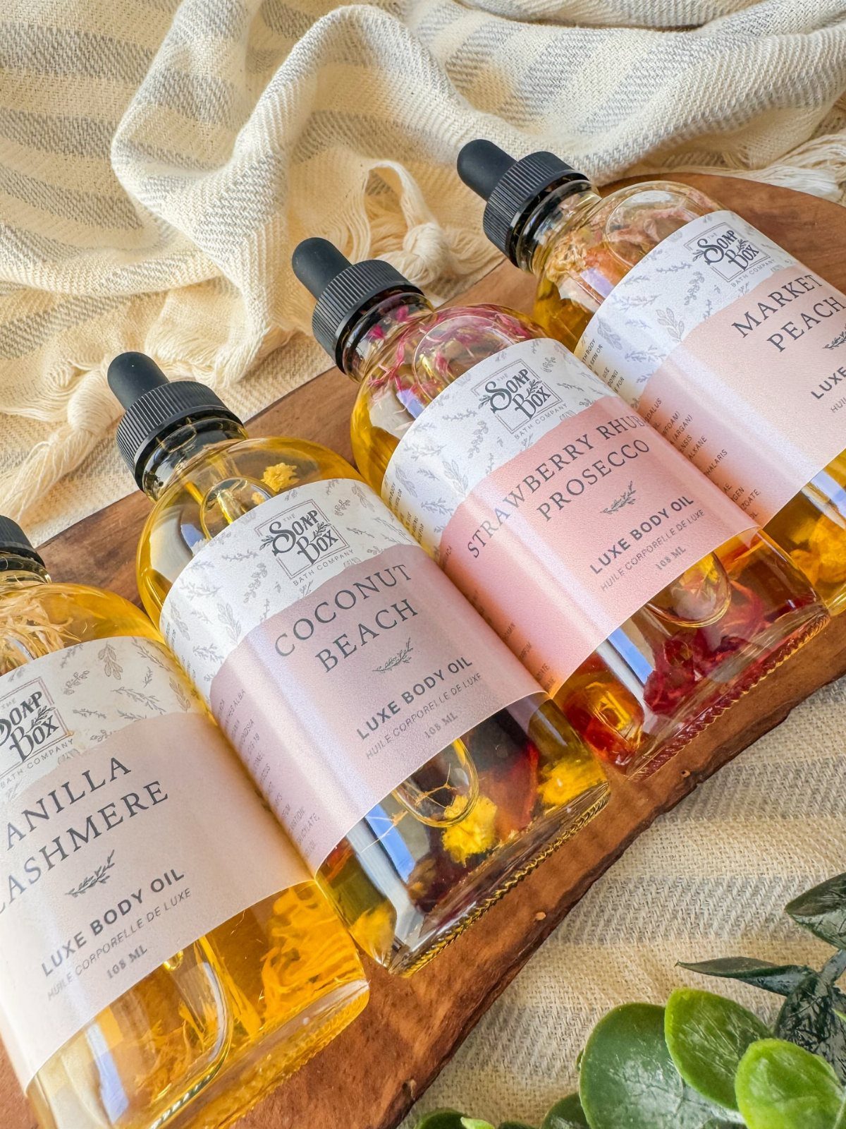 Four bottles of luxe body oil with botanical infusions on a wooden board.