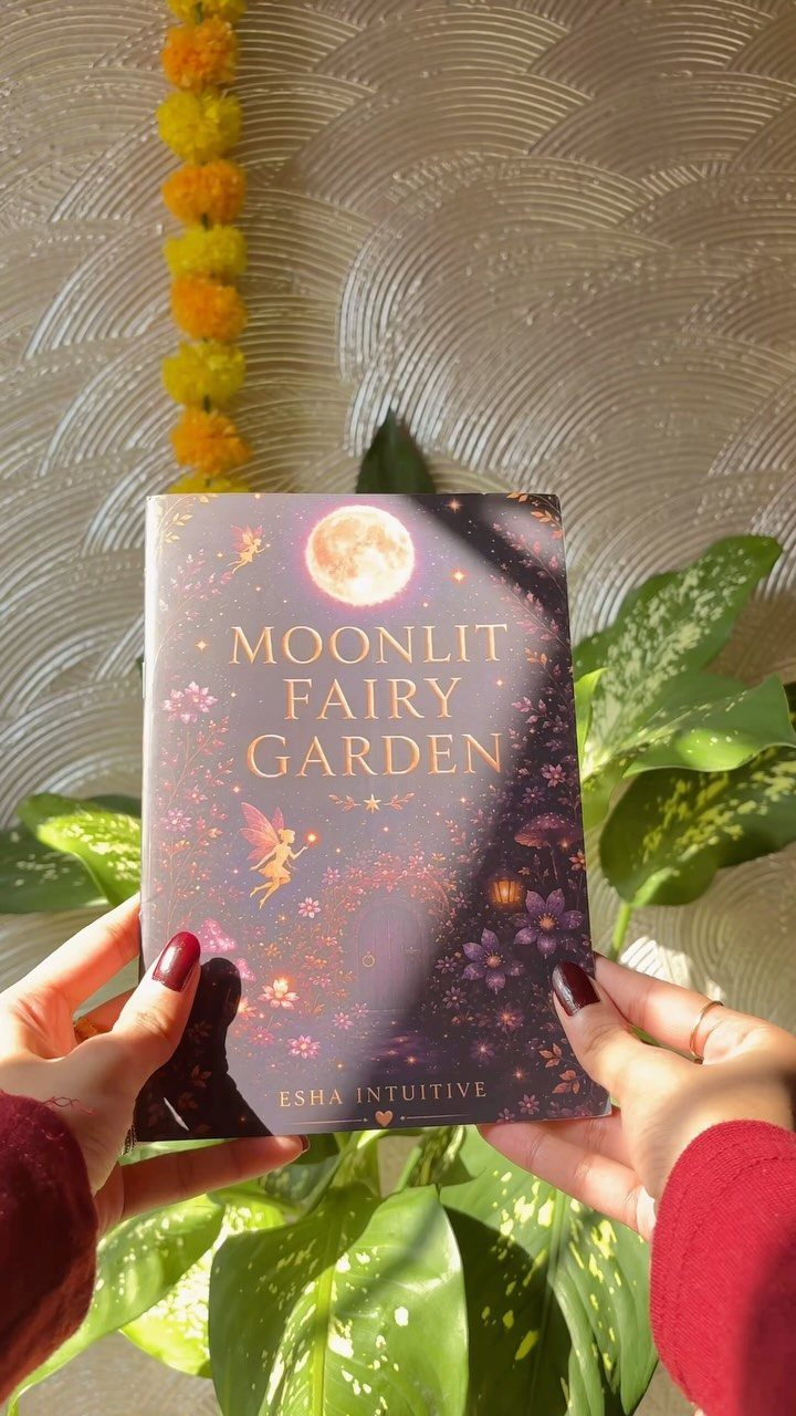 Hands holding a Moonlit Fairy Garden guided journal against green leaves and flowers.