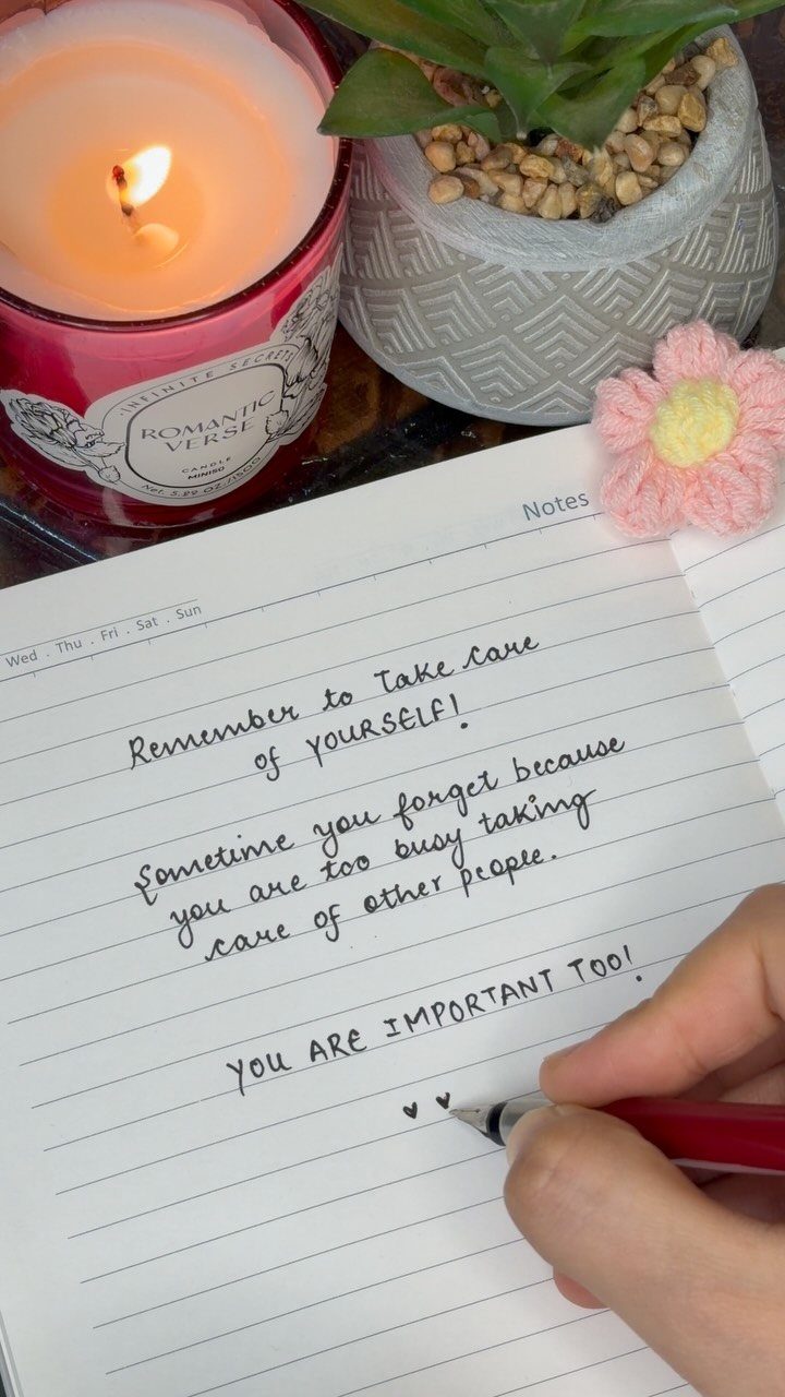 Hand writing a supportive message in a notebook next to a lit candle.