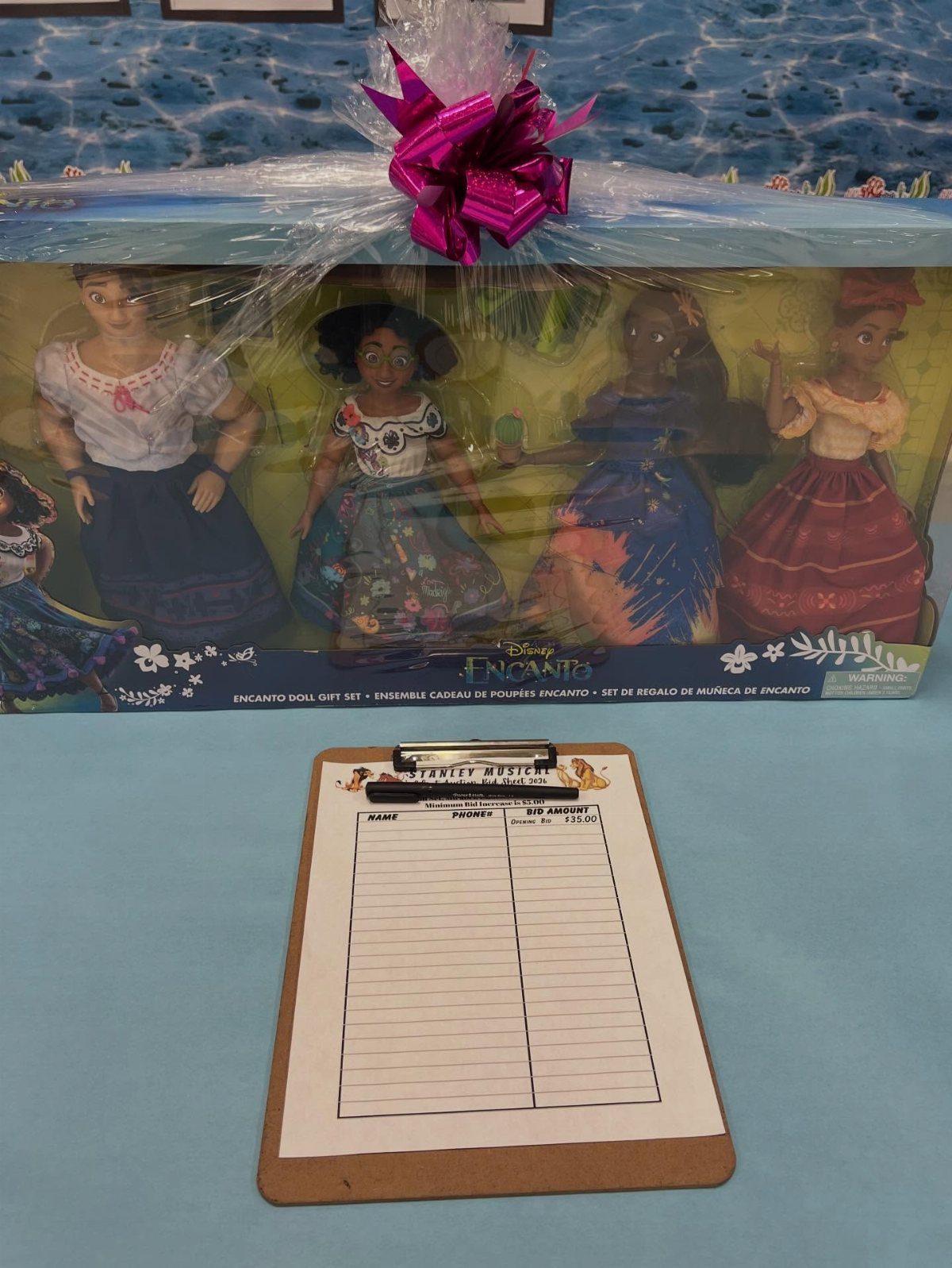 Encanto doll gift set wrapped in cellophane with a bid sheet on a clipboard.