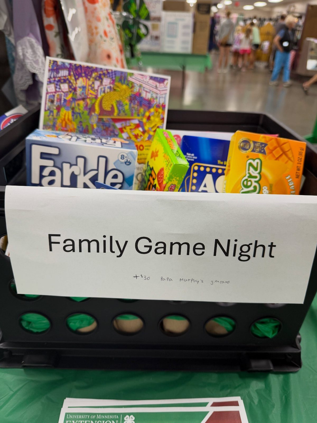 Family Game Night silent auction basket with board games and snacks on green tablecloth