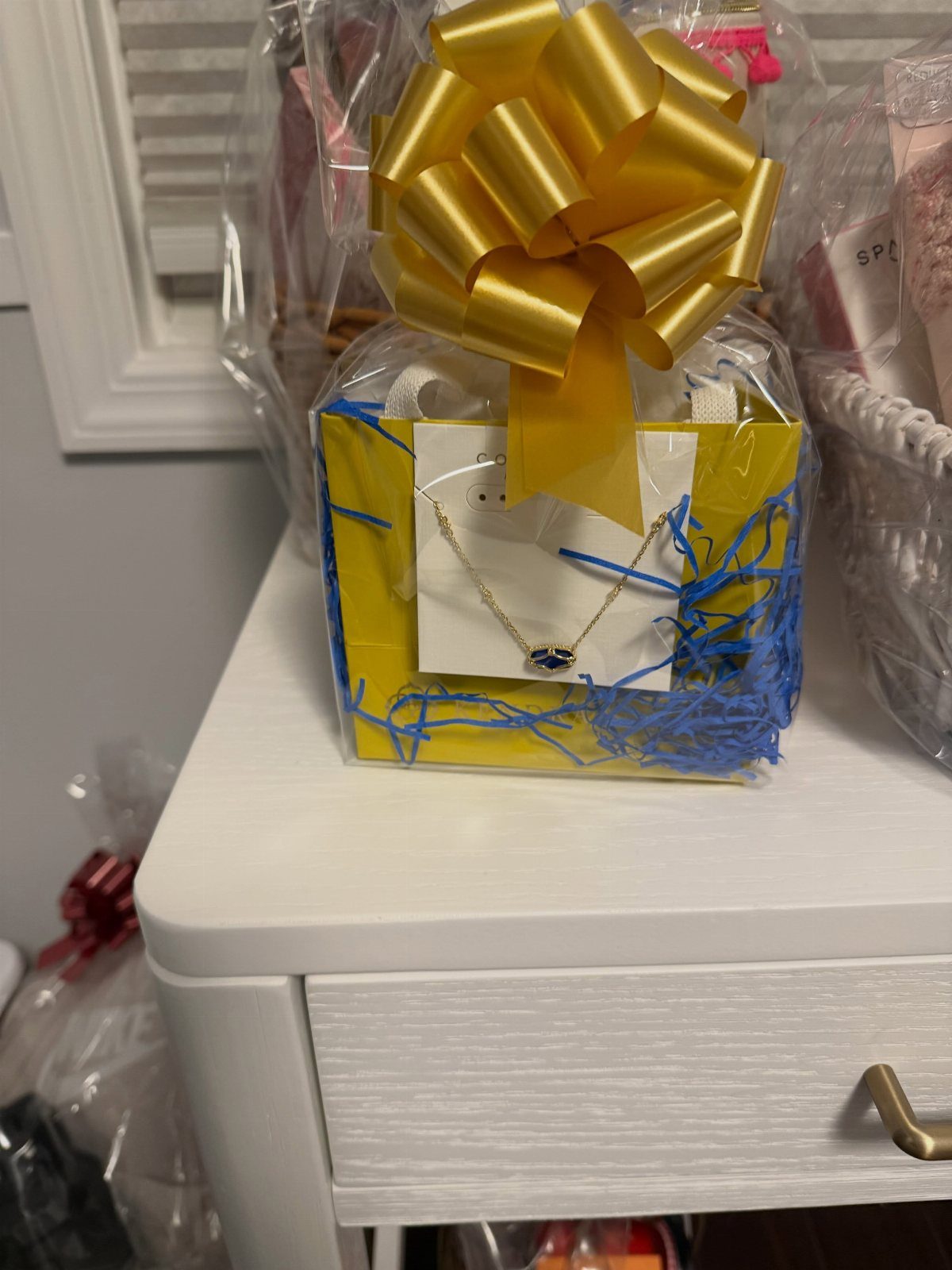 Gift basket wrapped in cellophane with a gold bow containing a blue eye necklace.