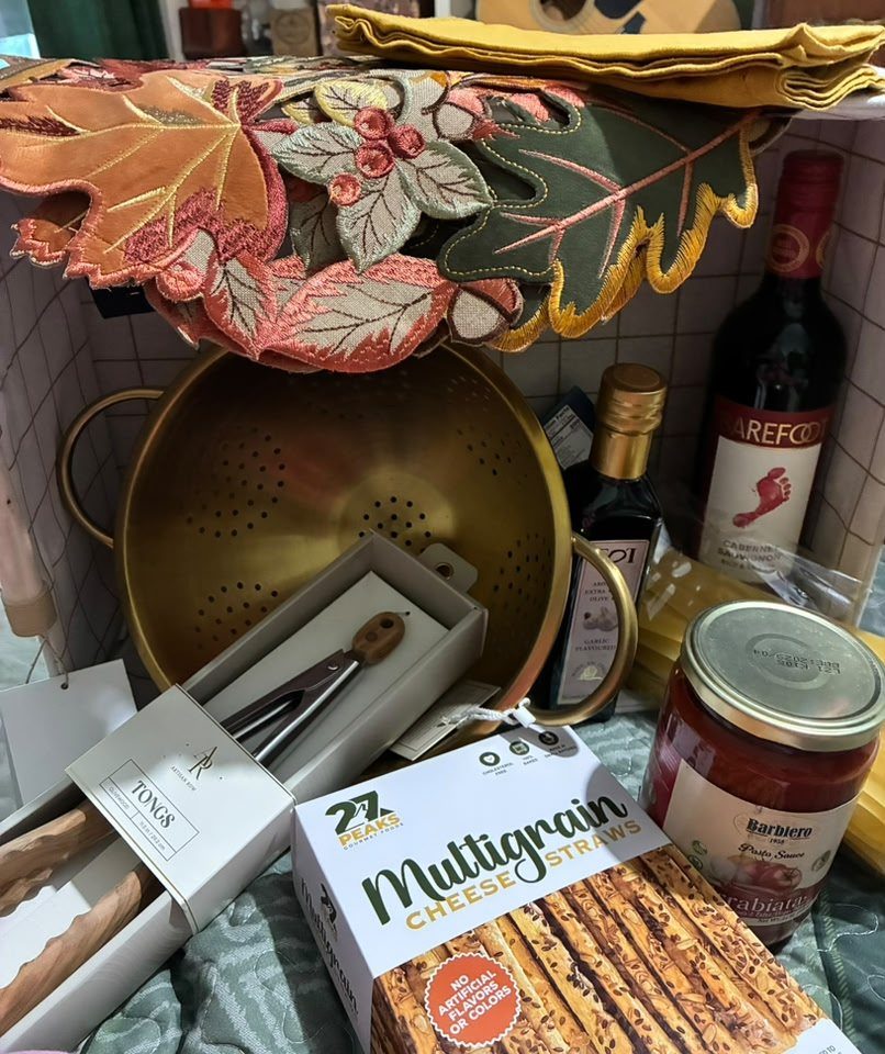 Gourmet cooking kit with gold colander, wine, pasta sauce, and cheese straws.
