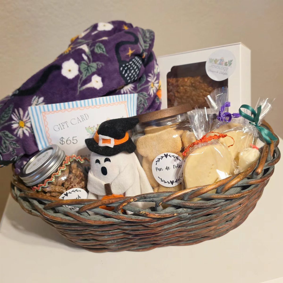 Woven gift basket with purple blanket, ghost plush, cookies, and a gift card.