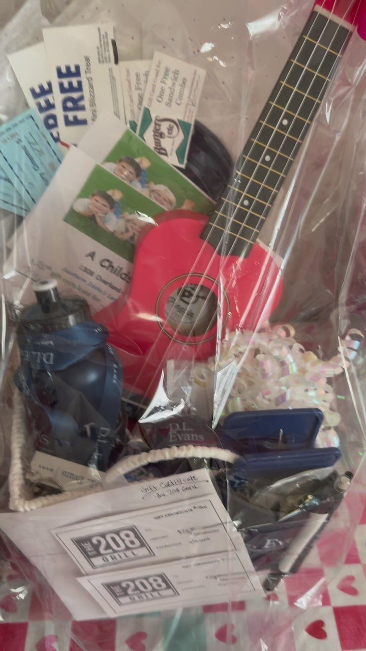 Gift basket wrapped in cellophane featuring a red ukulele and blue water bottle.