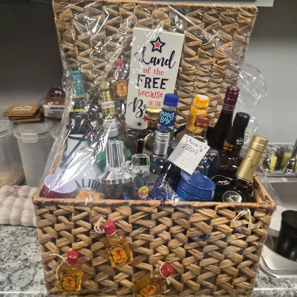 Woven gift basket filled with various liquor bottles and a patriotic sign.