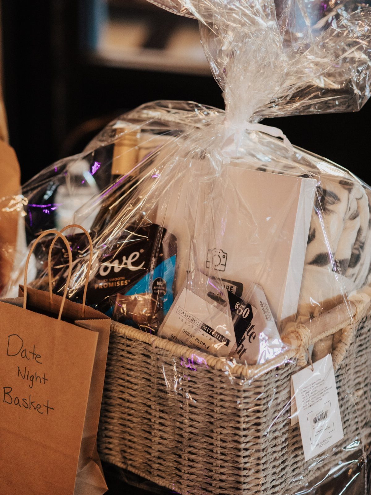 Wicker gift basket wrapped in cellophane with wine and chocolate for date night.