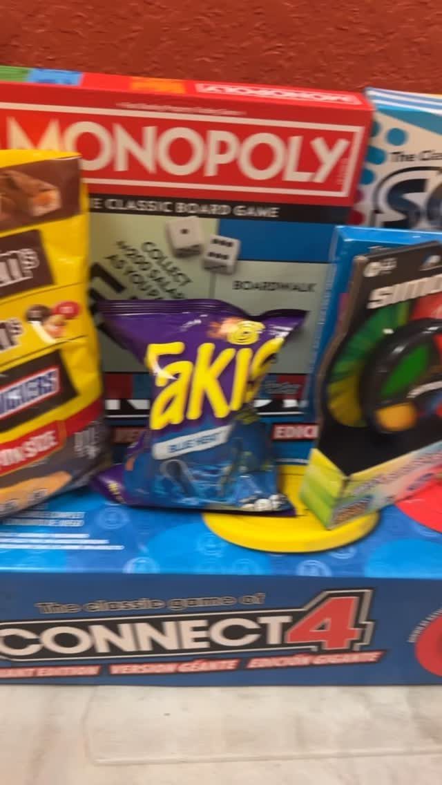 Board games and snacks including Monopoly and Connect 4 arranged as a gift basket.