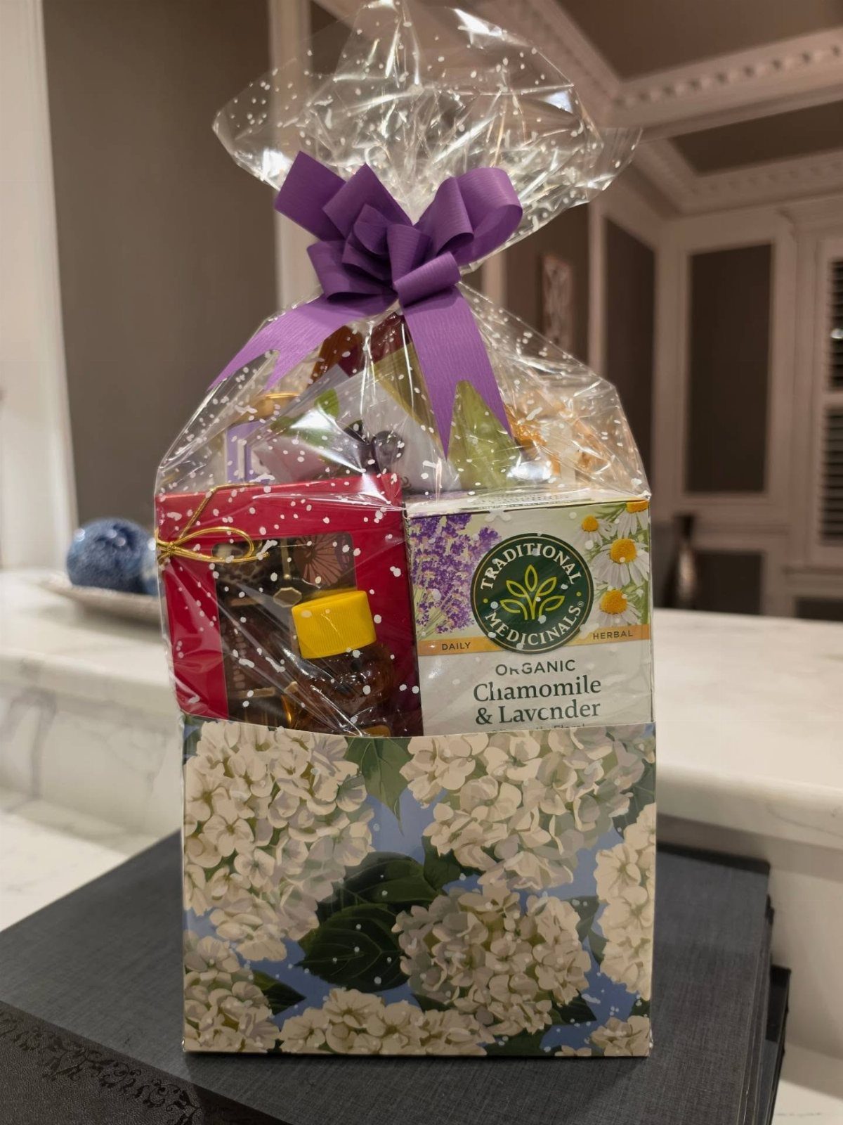 Gift basket wrapped in cellophane with a purple bow containing herbal tea boxes.