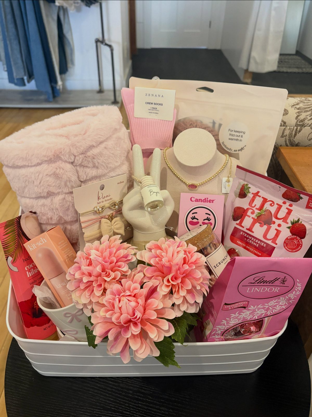 White gift basket filled with pink blanket, flowers, jewelry, and strawberry chocolates.