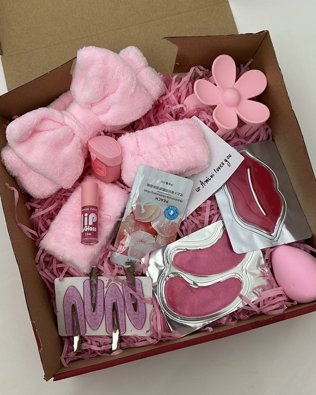 Pink skincare gift box with face masks, plush headband, and beauty accessories.