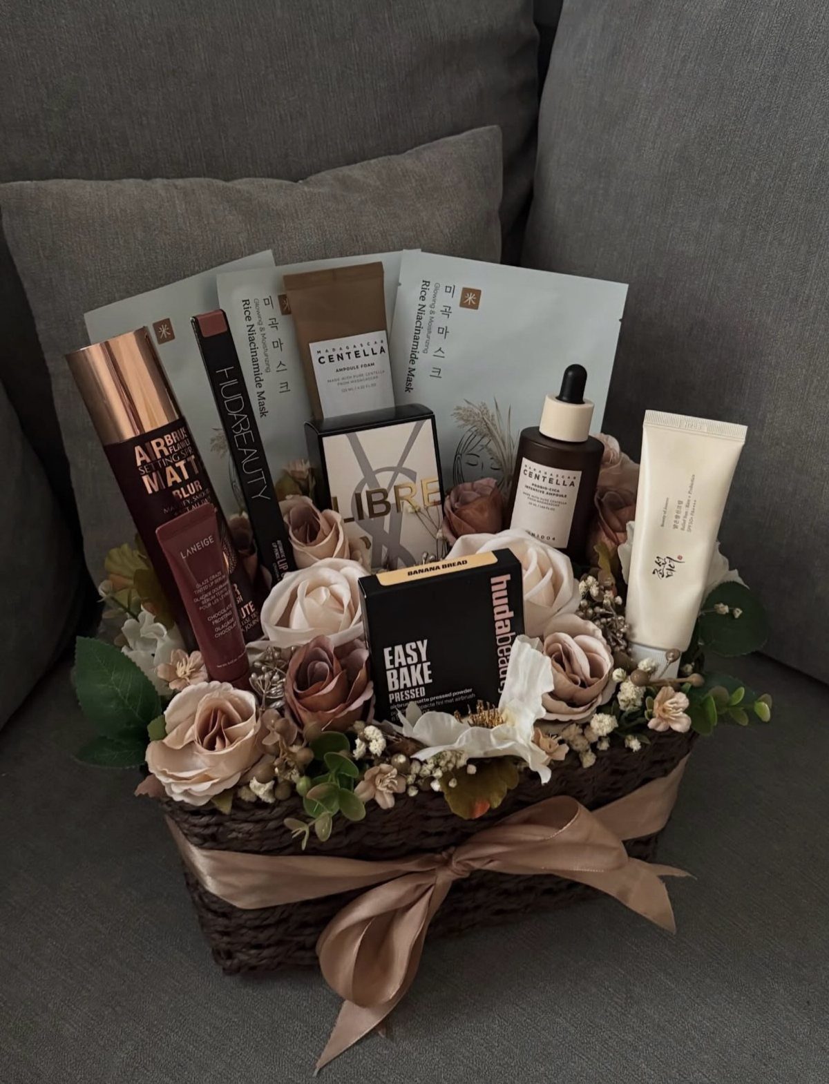 Wicker gift basket filled with skincare products and pale pink artificial roses.