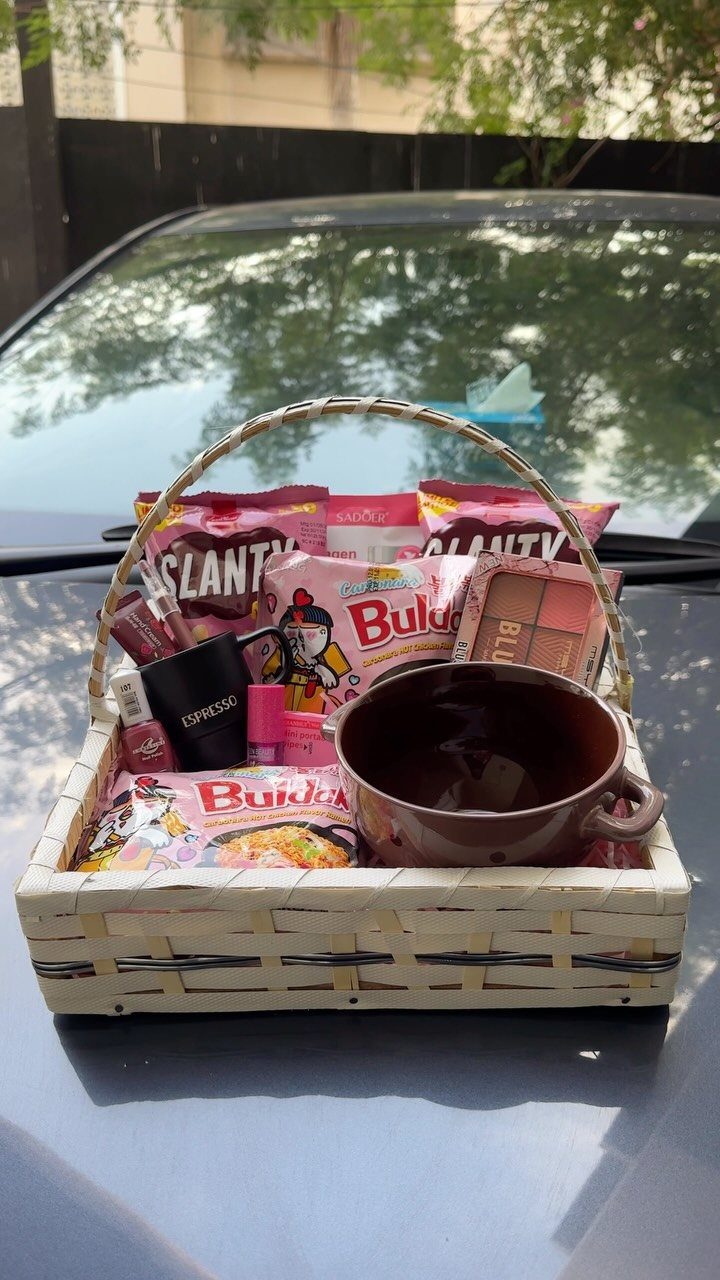 Woven gift basket with pink snacks, skincare bottles, and a brown ceramic bowl.