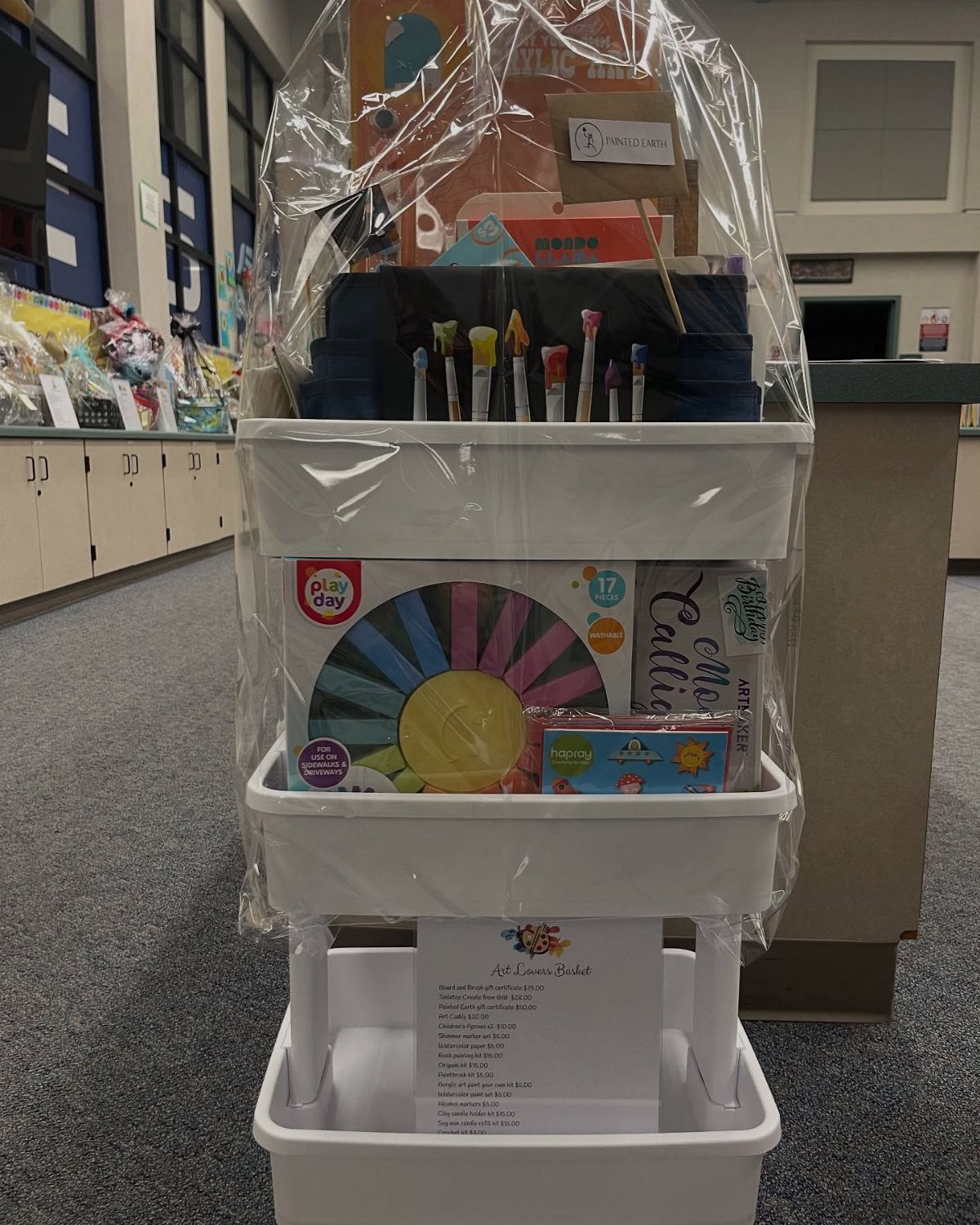 Art supplies in a white rolling cart wrapped in clear cellophane for a raffle.