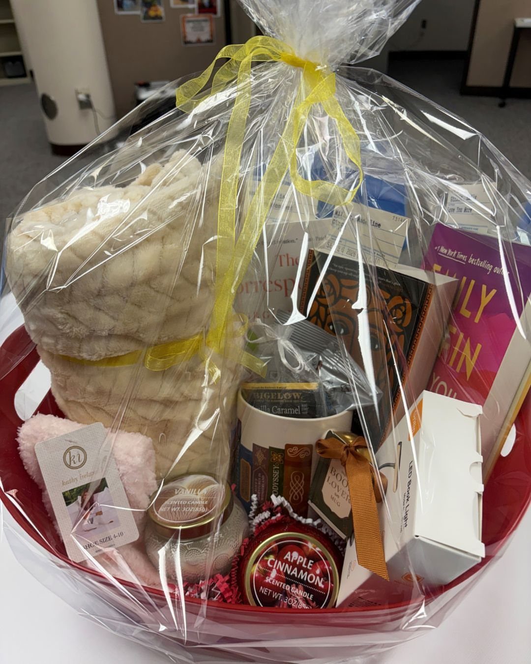 Gift basket with books, a white blanket, and a mug wrapped in cellophane.