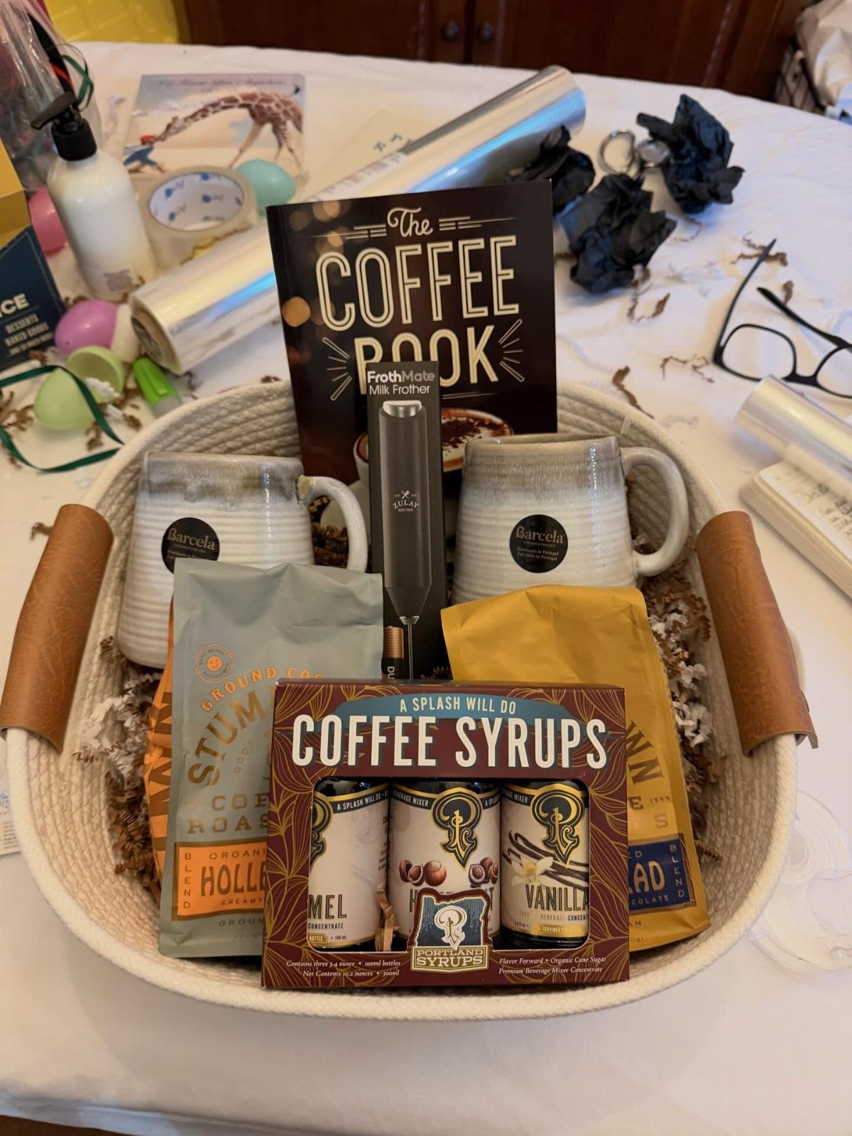 Coffee themed gift basket with mugs, coffee syrups, beans, and a coffee book.