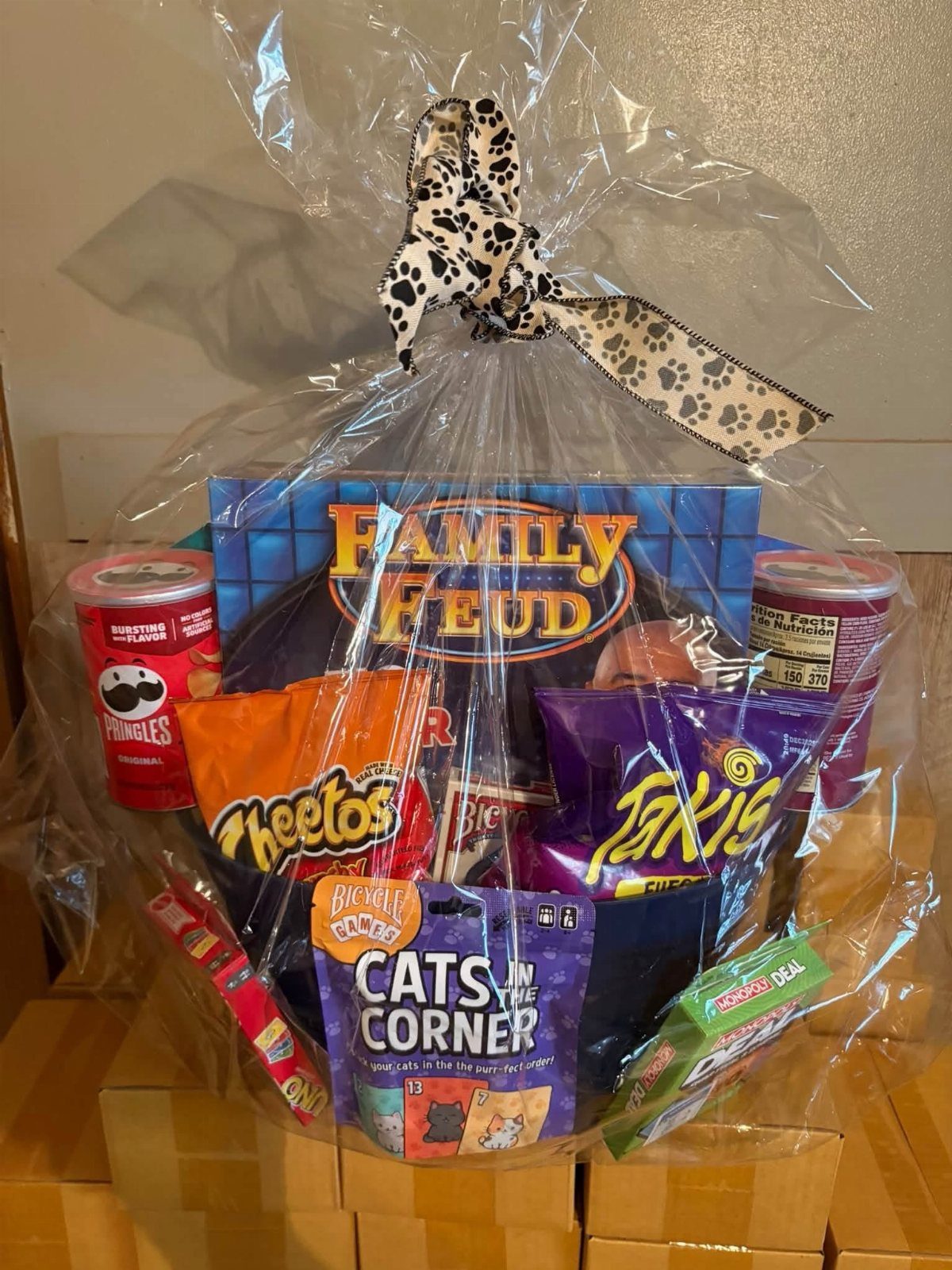 Gift basket with Family Feud board game, snacks, and cards wrapped in cellophane.