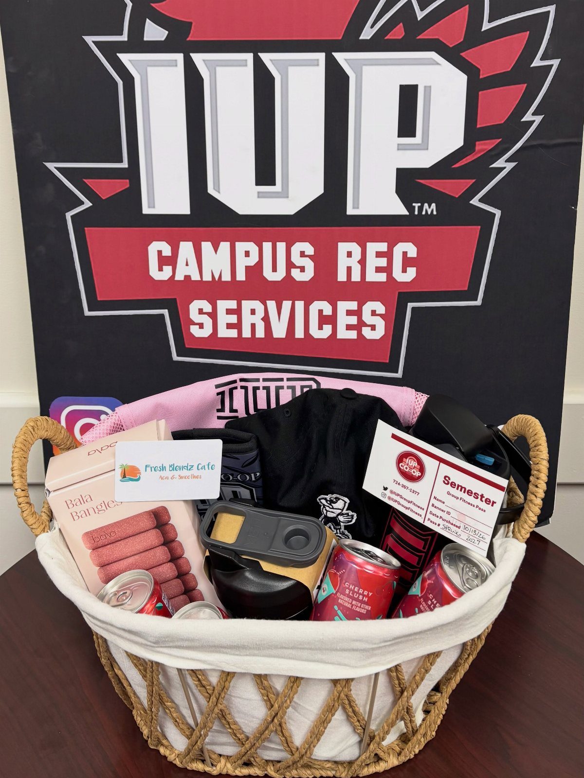 Fitness gift basket with water bottle and gym gear before a campus rec banner.