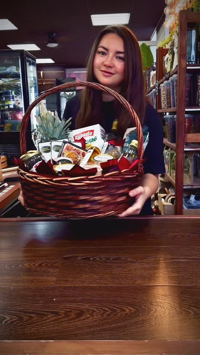 Woman holding a wicker gift basket filled with gourmet food and a plant.