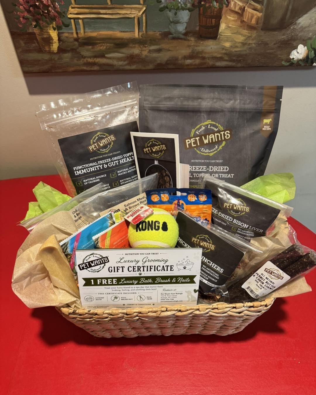 Wicker gift basket filled with dog treats, toys, and a grooming gift certificate.