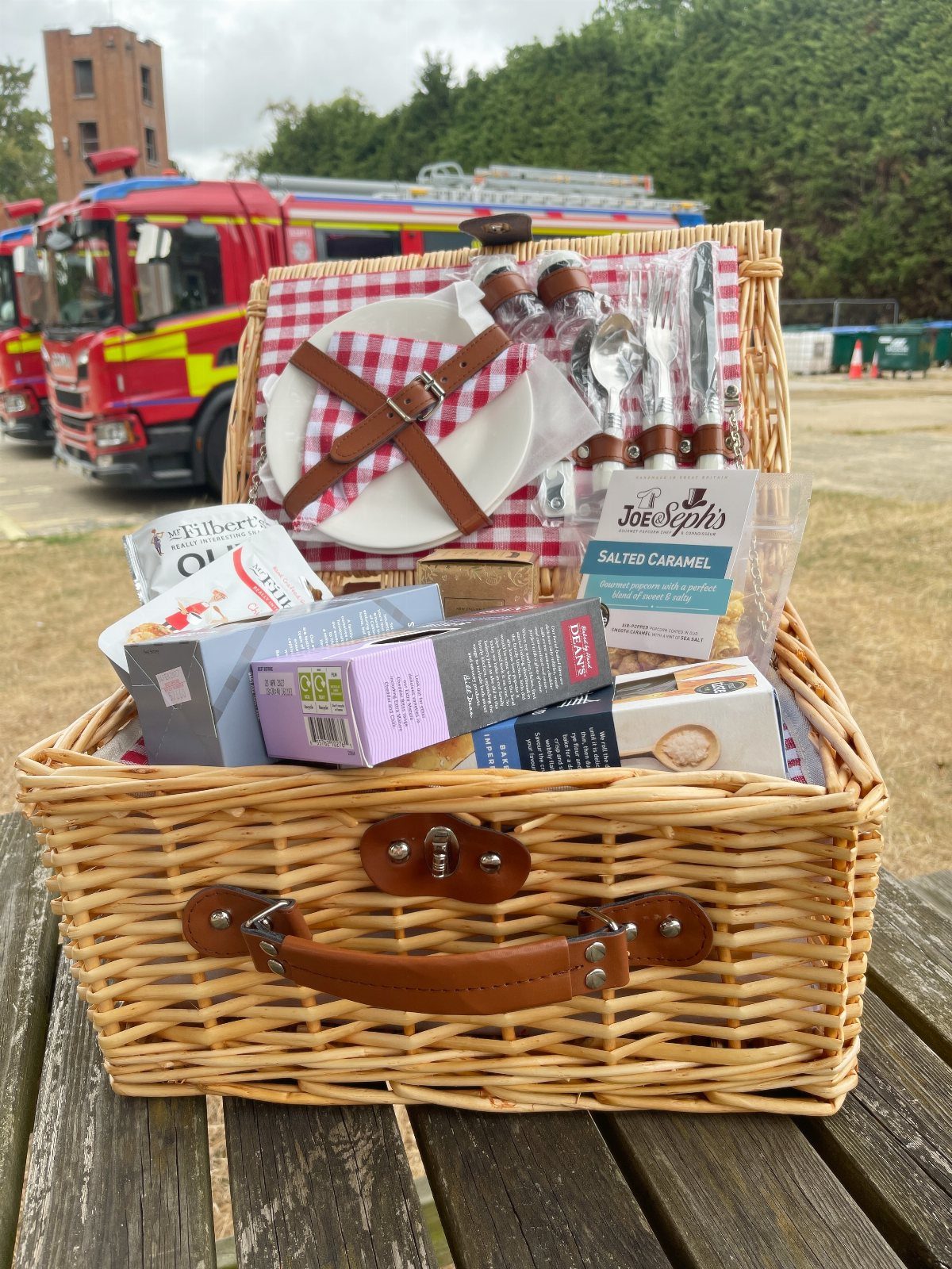 Wicker picnic basket filled with gourmet snacks and plates on a wooden table.