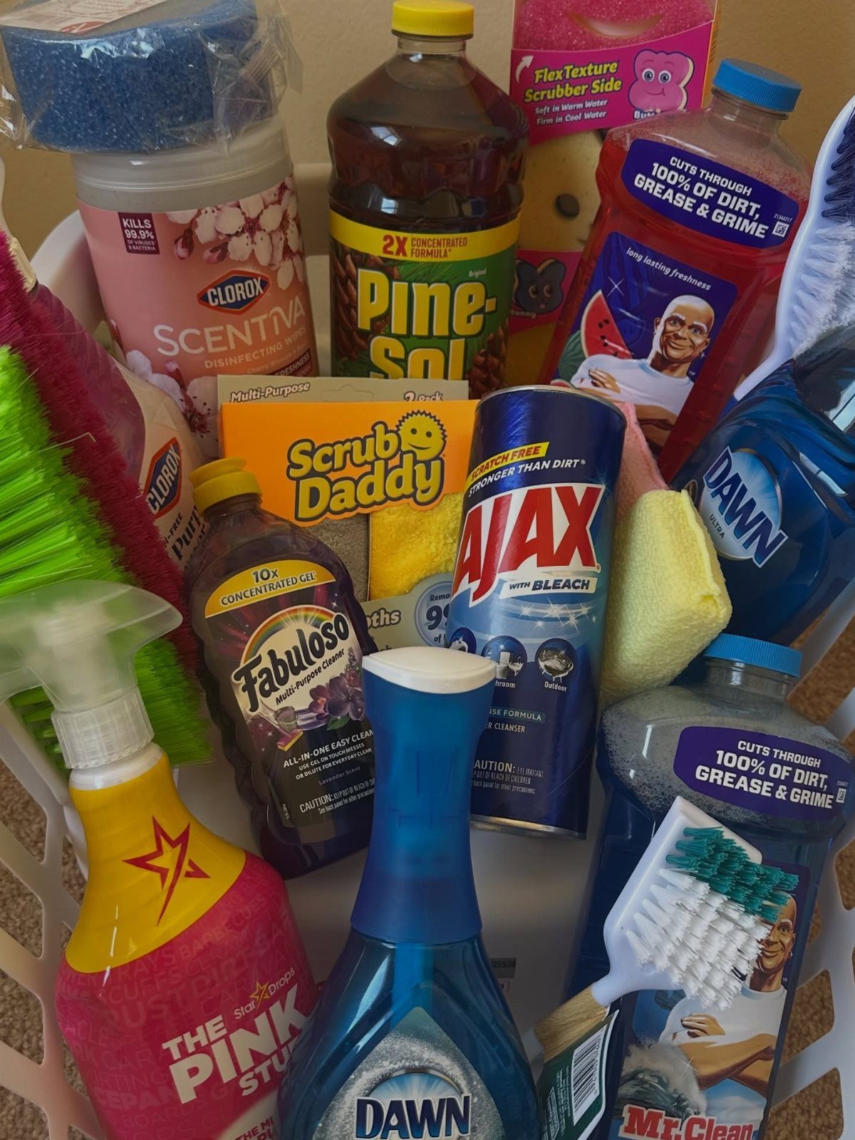Cleaning supplies including spray bottles and sponges arranged in a white plastic basket.