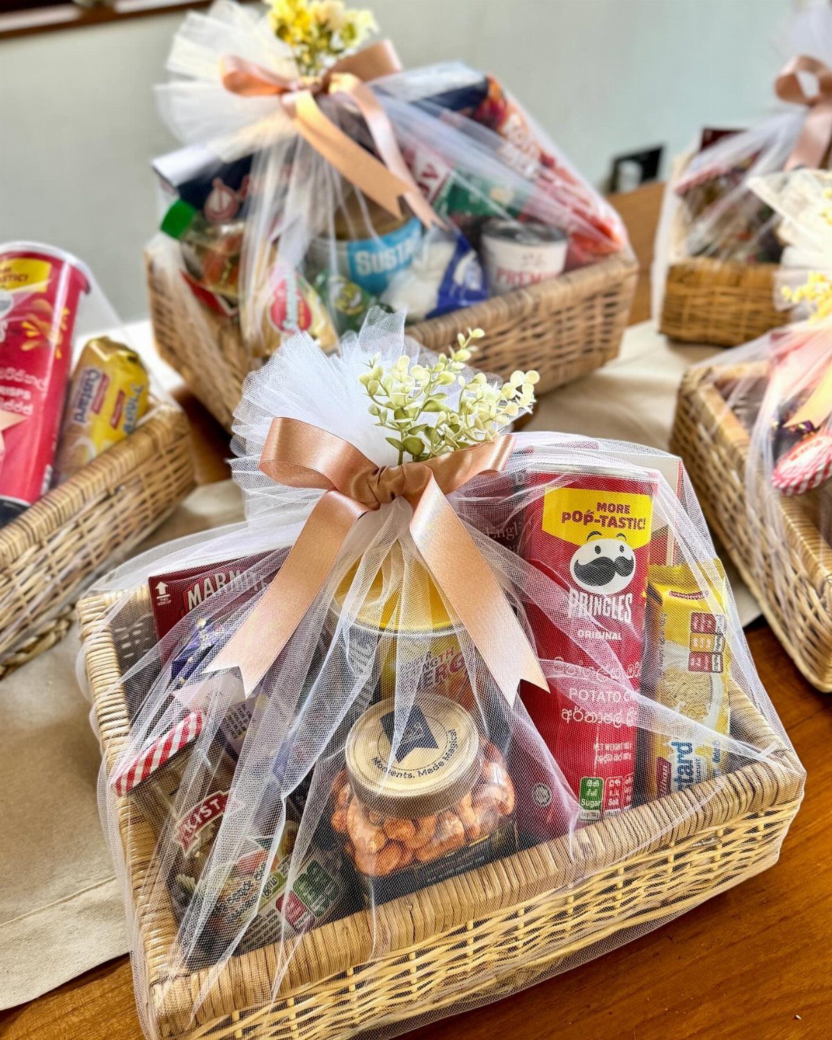 Woven gift baskets filled with snacks and wrapped in white tulle and ribbons.