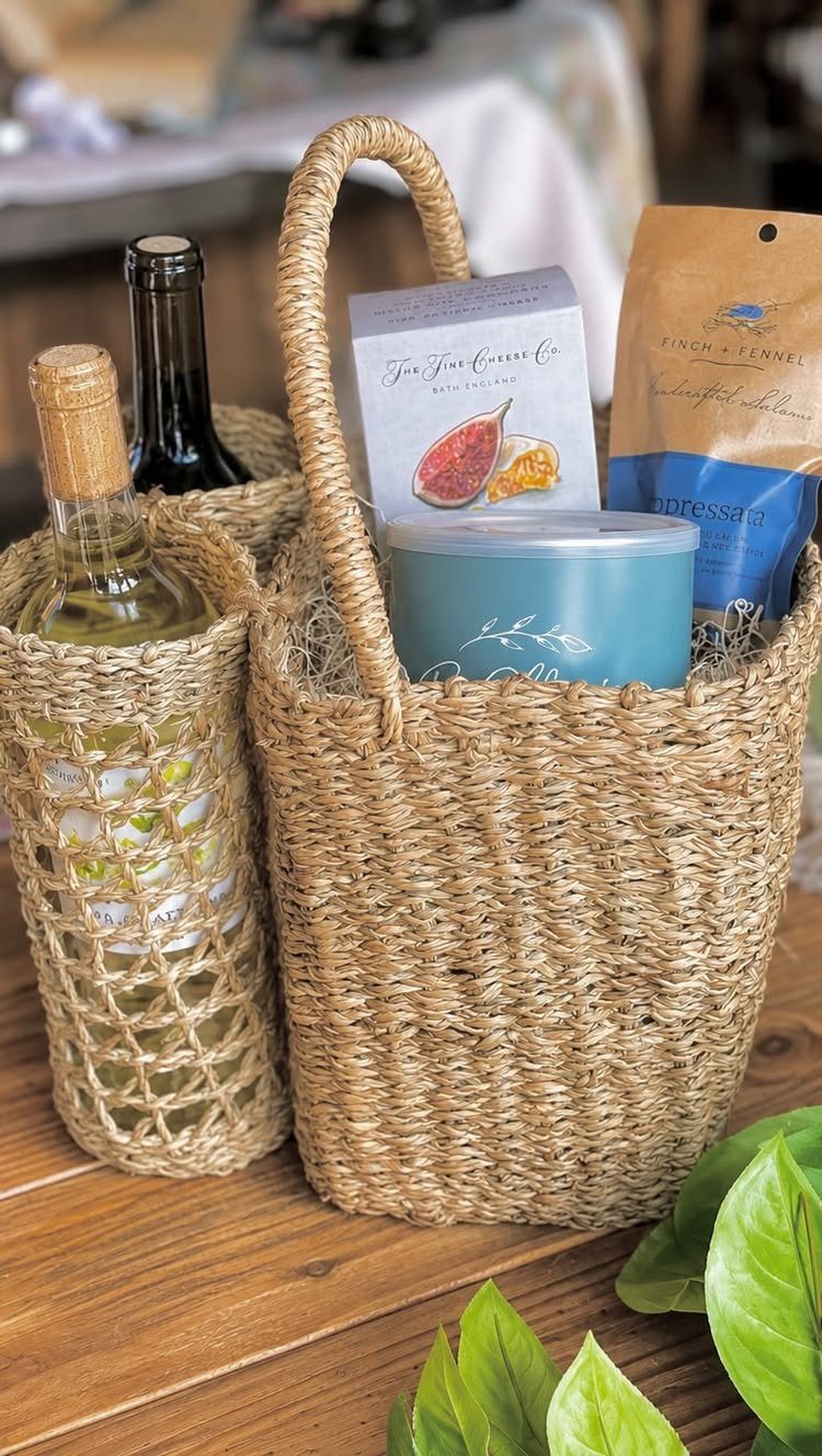Woven straw baskets containing a bottle of white wine, a candle, and snacks.