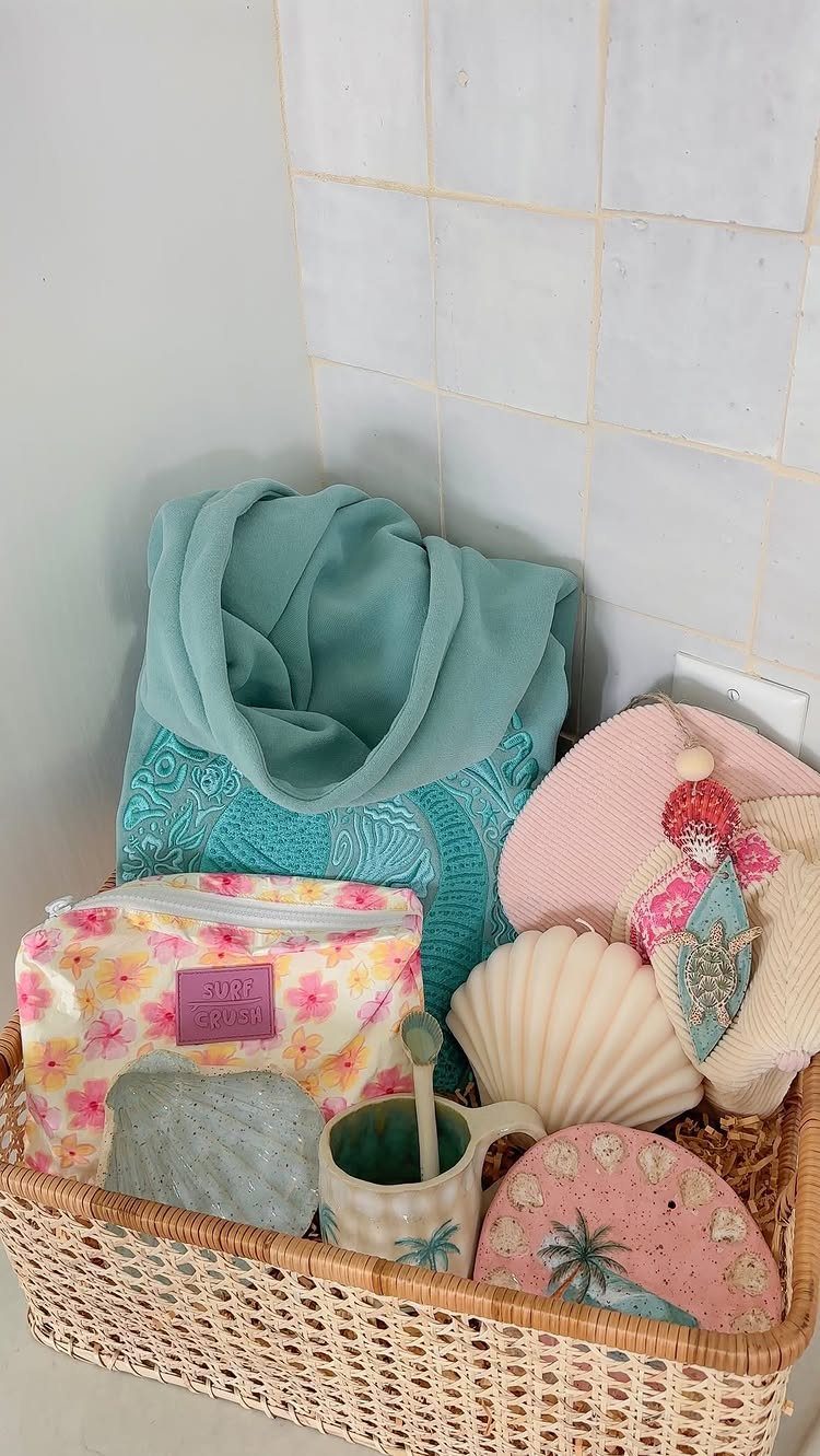 Woven basket filled with teal towels, seashell bowl, and beach-themed accessories.