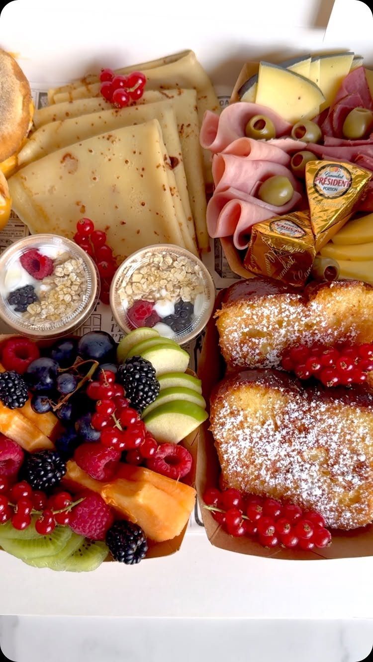 Breakfast box with crepes, fresh fruit, yogurt parfaits, meats, cheeses, and cakes.