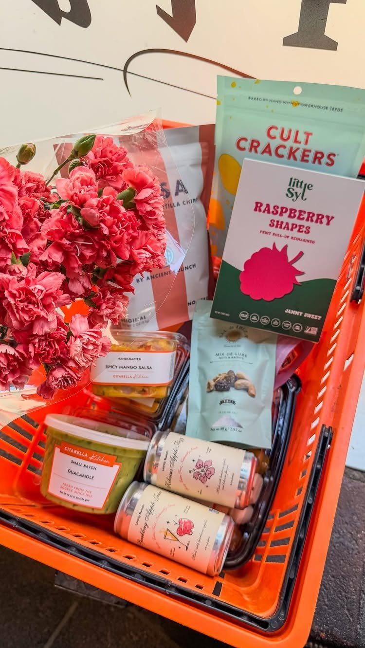 Orange basket filled with gourmet crackers, sweets, jars, and pink carnations.