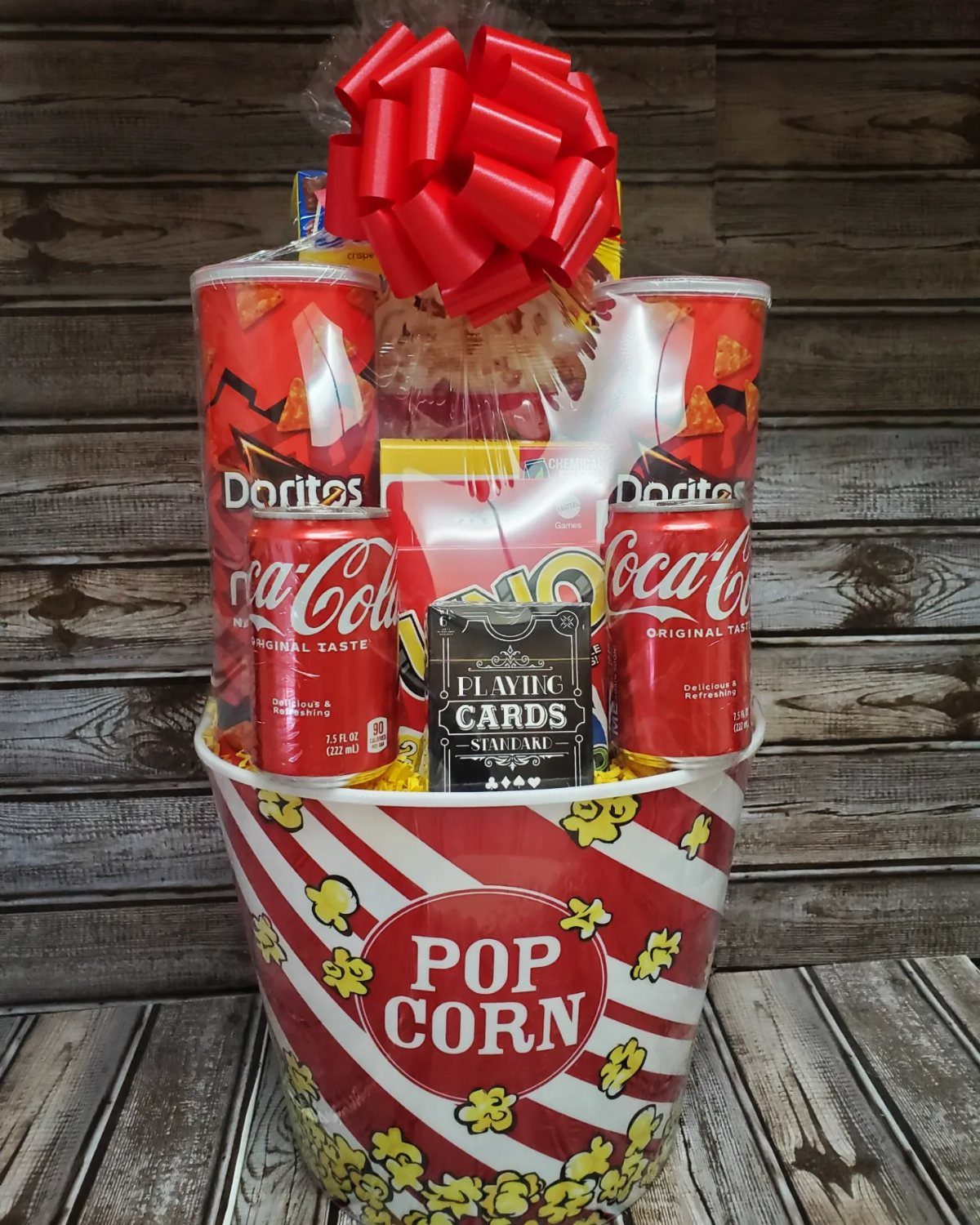 Movie night gift basket in a popcorn bucket with snacks and red bow.