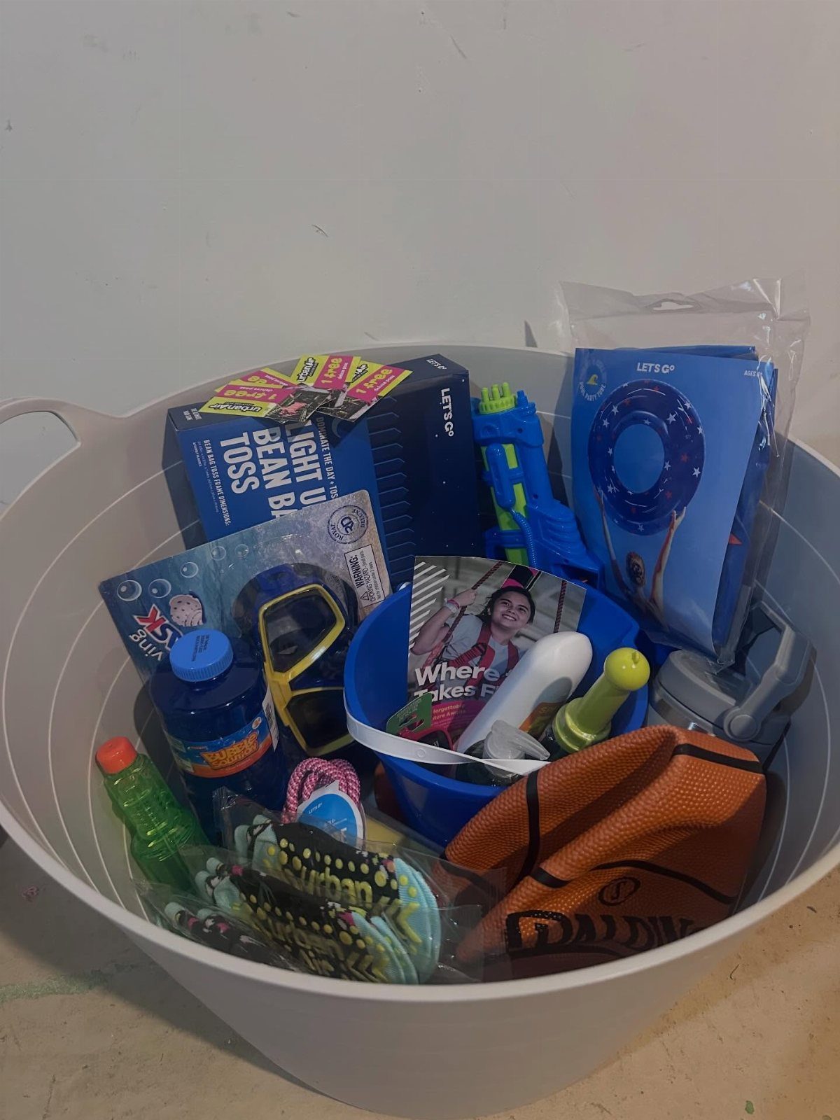 White tub filled with summer toys, including a basketball, snorkel mask, and water gun.