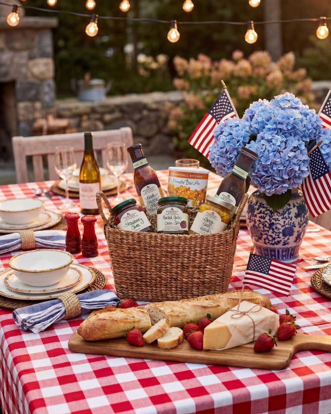 Gourmet gift basket with wine, cheese, and baguette on a red checkered tablecloth.