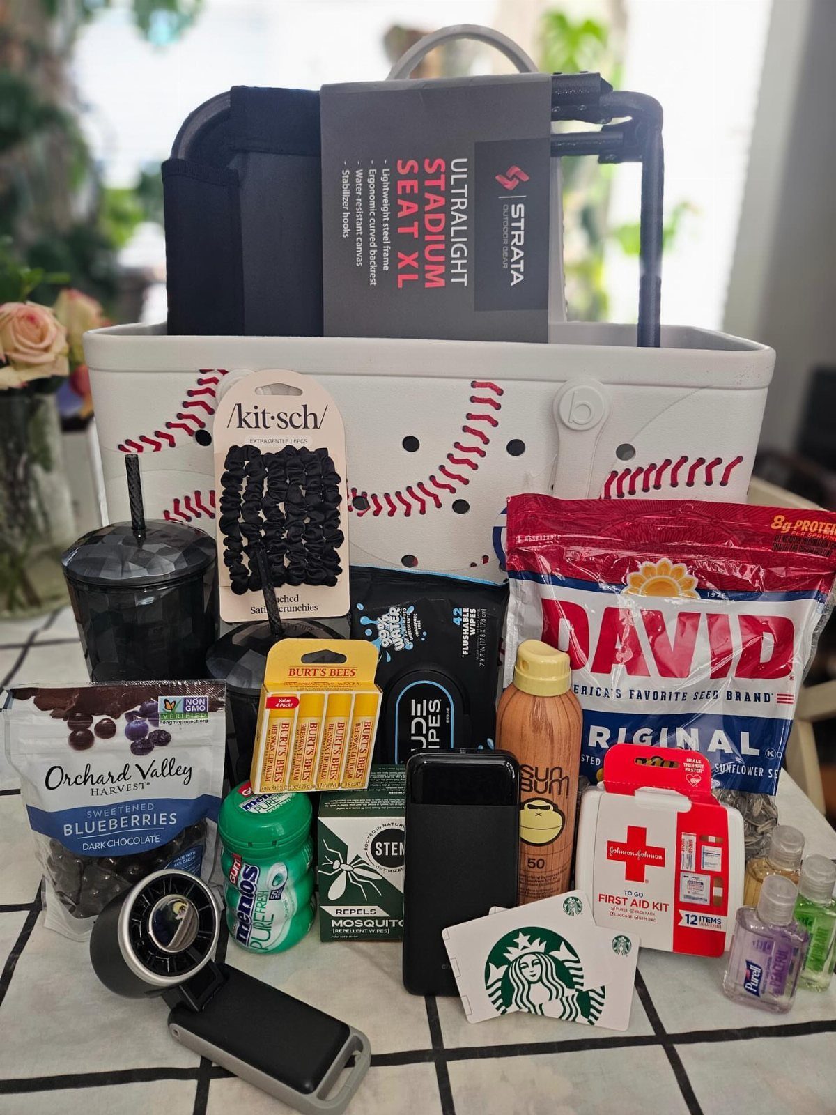 Baseball themed gift basket with stadium seat, snacks, and outdoor essentials on tile.