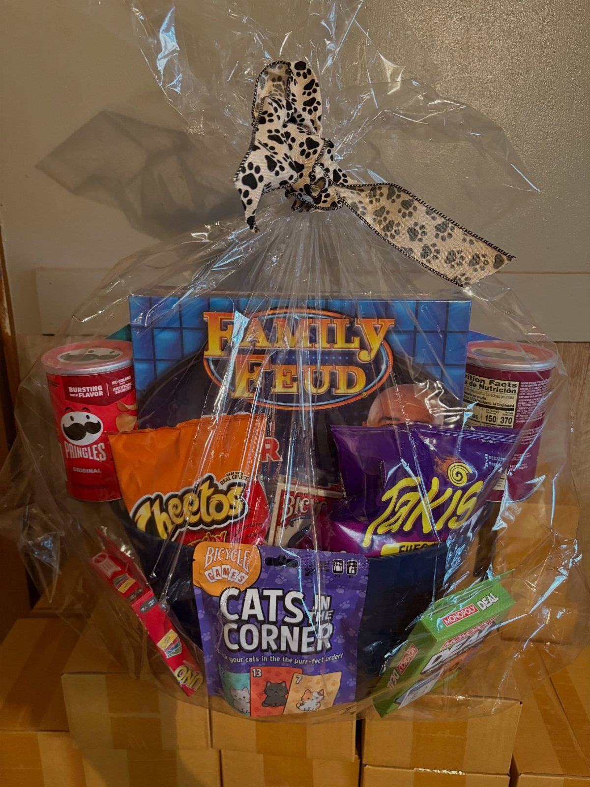 Gift basket with Family Feud game, Cheetos, Takis, and Pringles wrapped in cellophane.