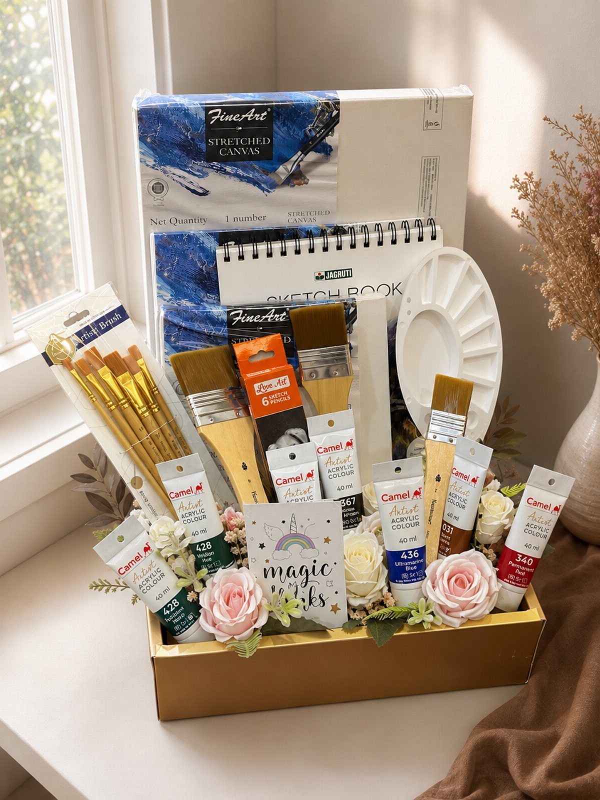 Art supplies in a gold basket with canvas, sketchbook, brushes, and paint tubes.