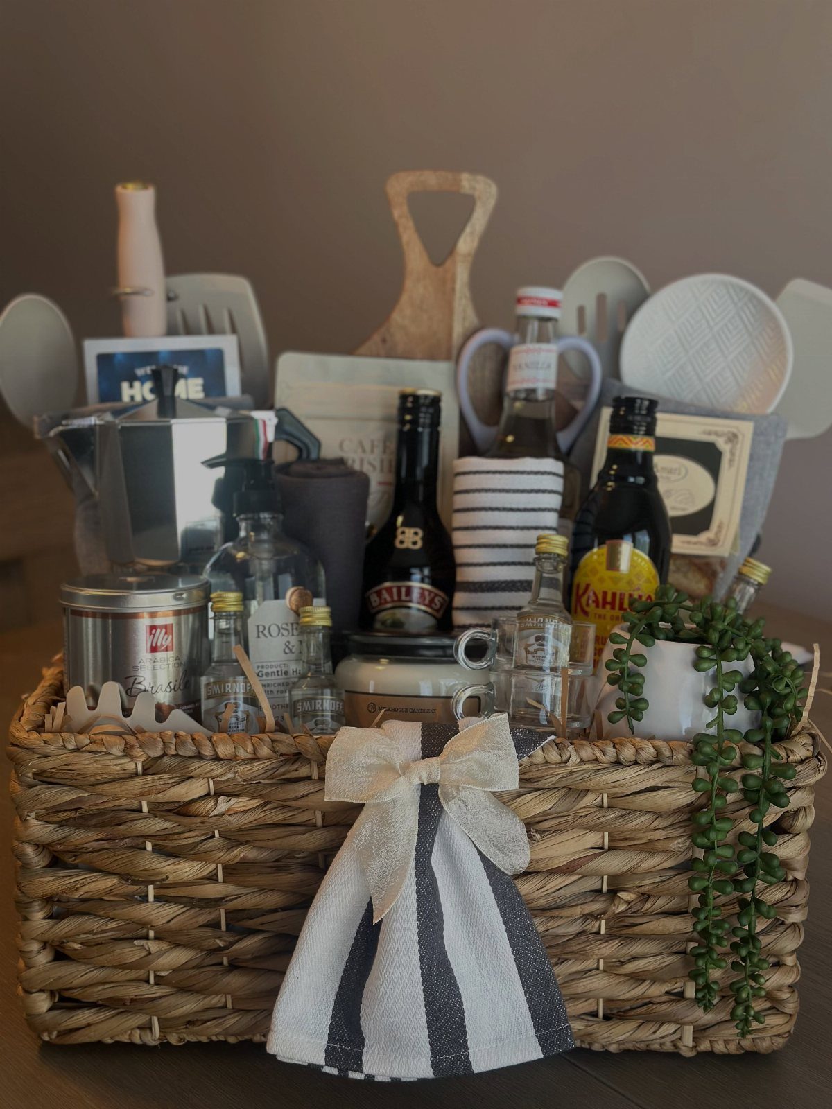 Woven gift basket containing a Moka pot, bottled beverages, and a striped cloth.