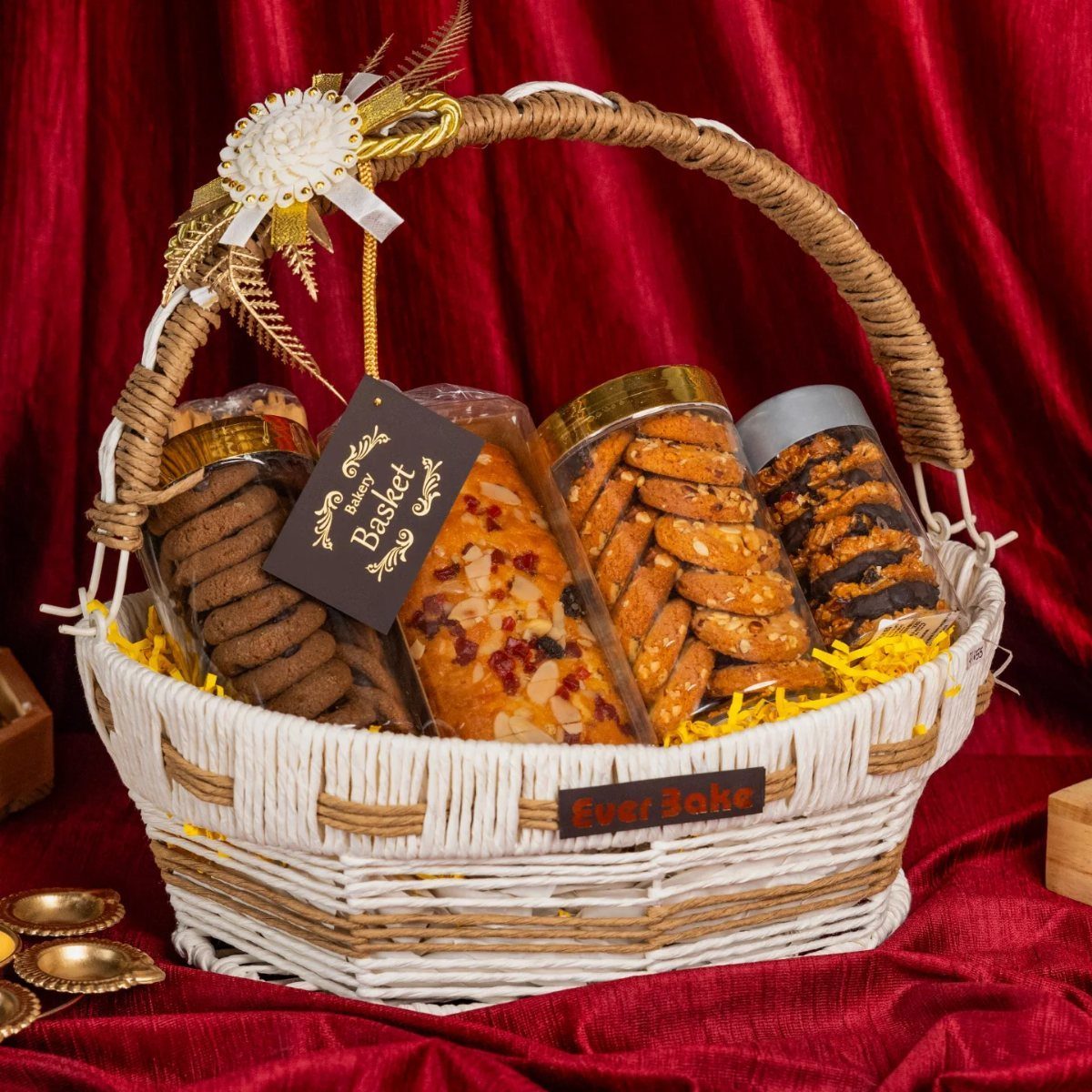 White wicker gift basket filled with assorted cookies and biscuits against red fabric.