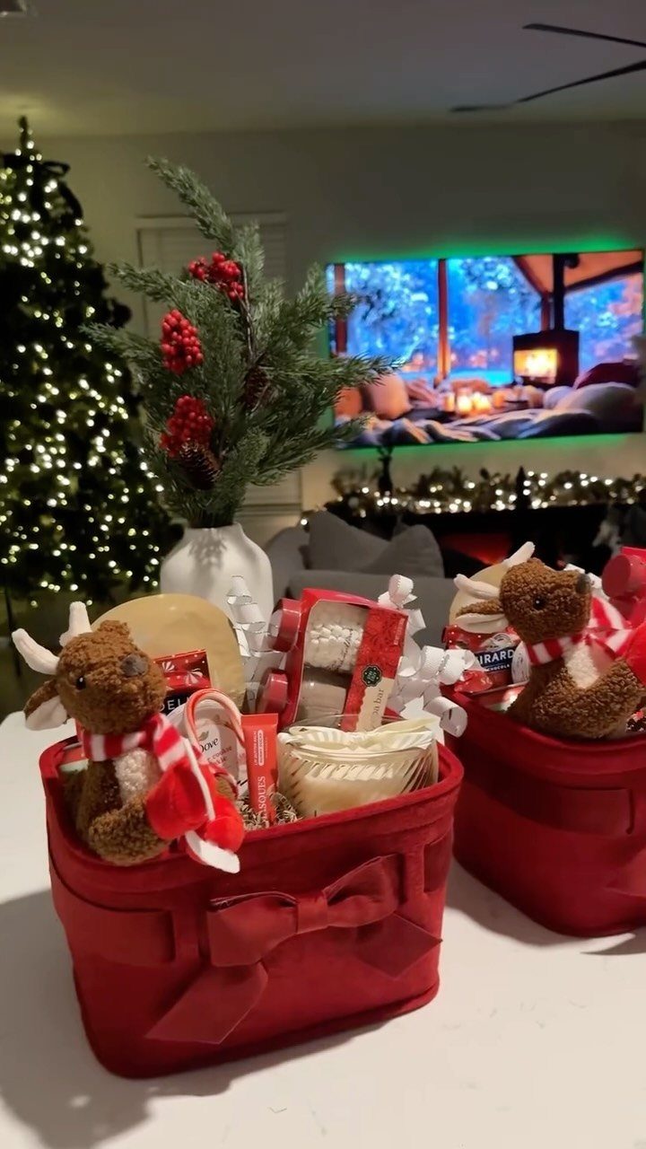 Red holiday gift baskets filled with treats and plush reindeer near a Christmas tree