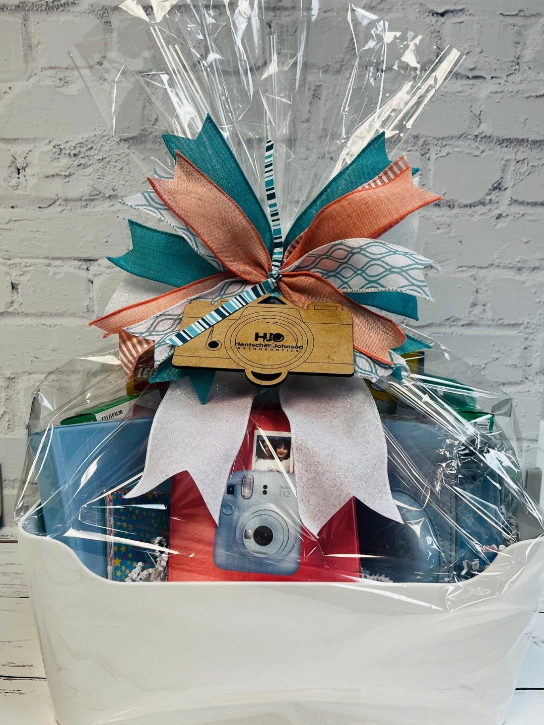 Gift basket wrapped in cellophane with a blue instant camera and large bow.