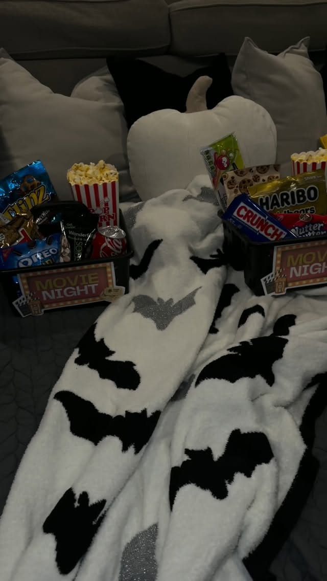 Movie night baskets with popcorn and candy on a sofa with a bat blanket.