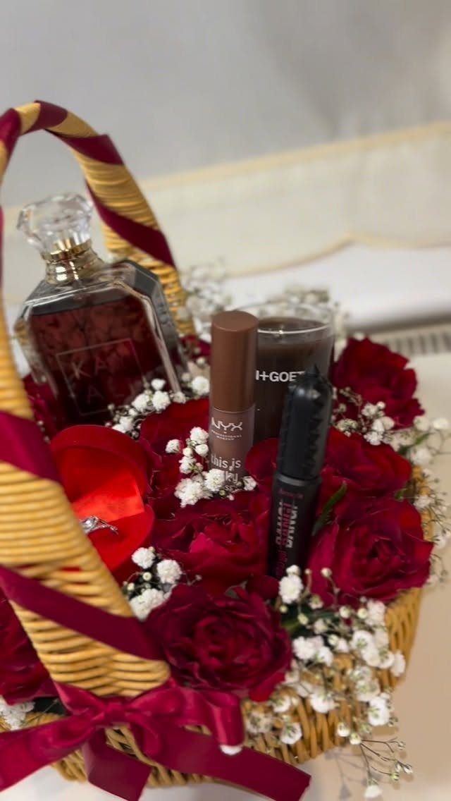 Wicker gift basket filled with red roses, perfume, and makeup products with ribbons.